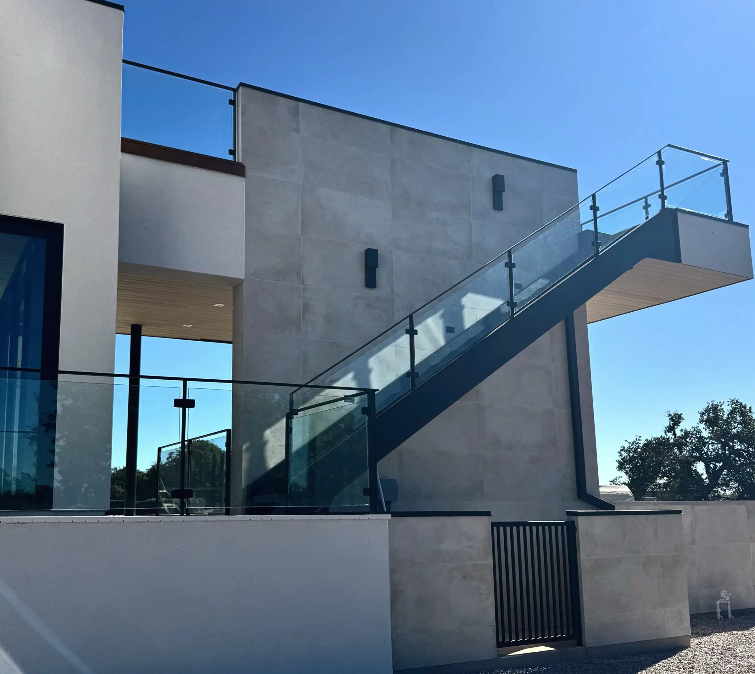Glass railings with black posts running along an exterior staircase and upper terrace of a modern rendered and concrete-panel building.
