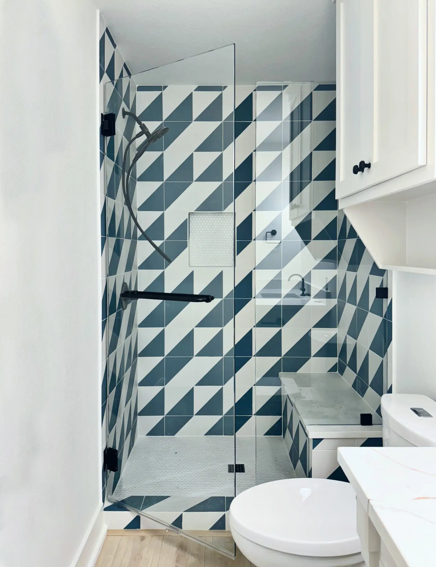 A frameless inline glass shower door and panel in a bathroom tiled in bold blue and white geometric tile, with black hardware.