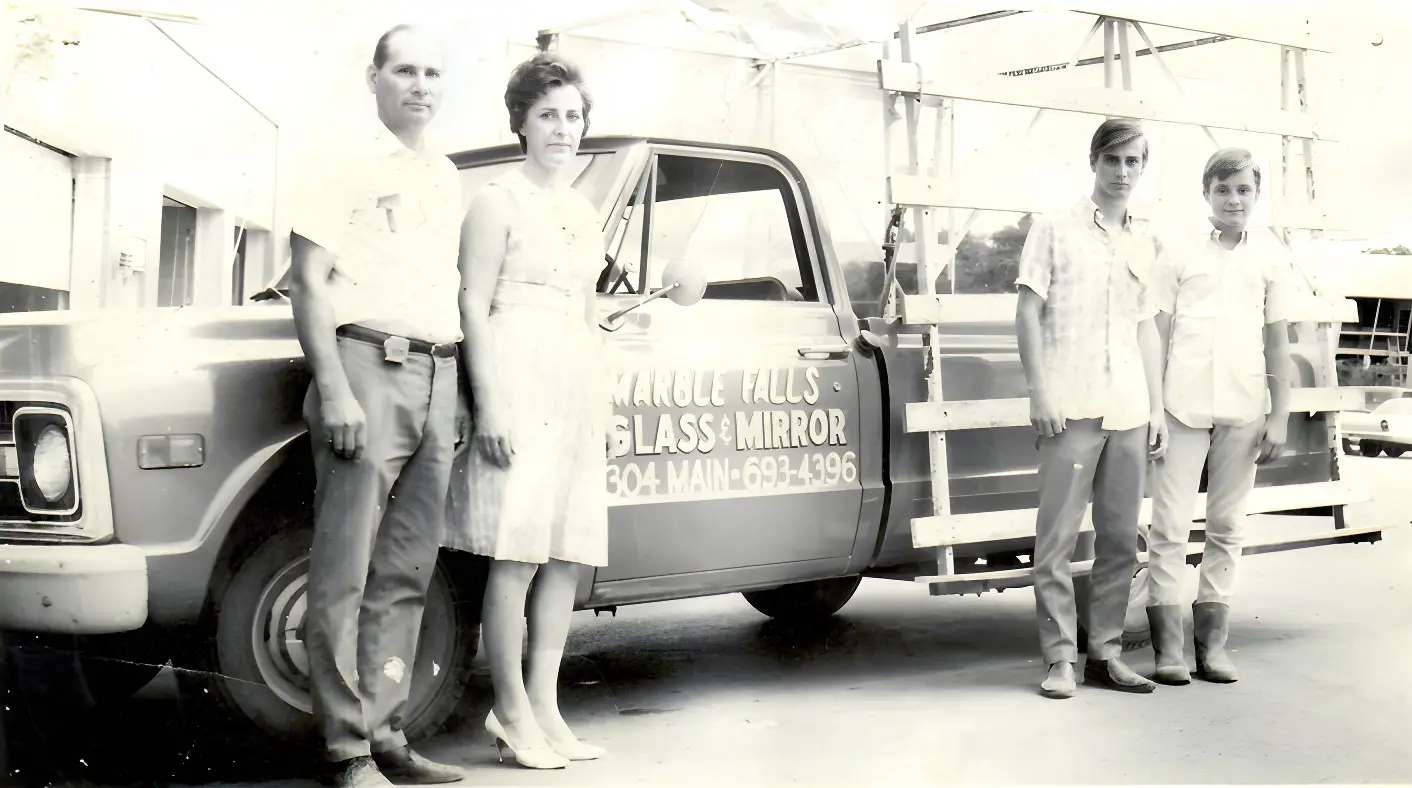Four people standing beside the original Marble Falls Glass and Mirror pickup, its door lettered 304 MAIN and a glass rack built onto the bed.
