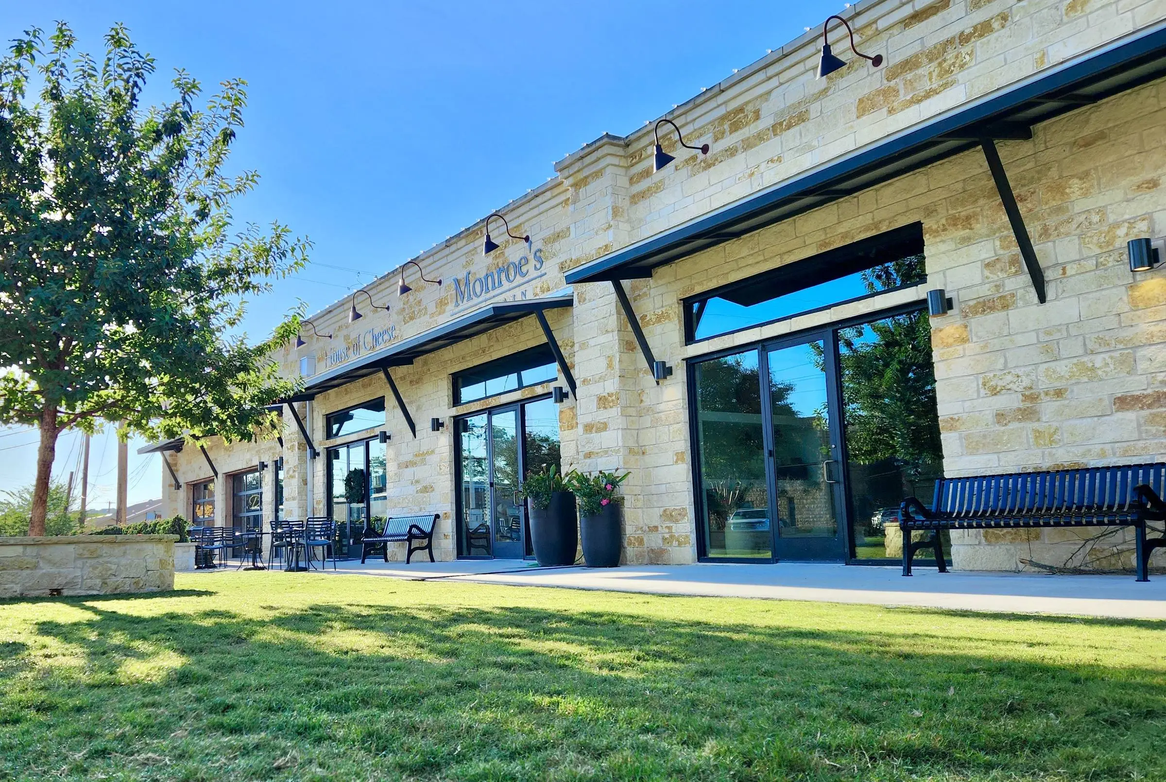 Black-framed glass storefront and entry doors set into a Texas limestone building, with metal awnings over the walkway.