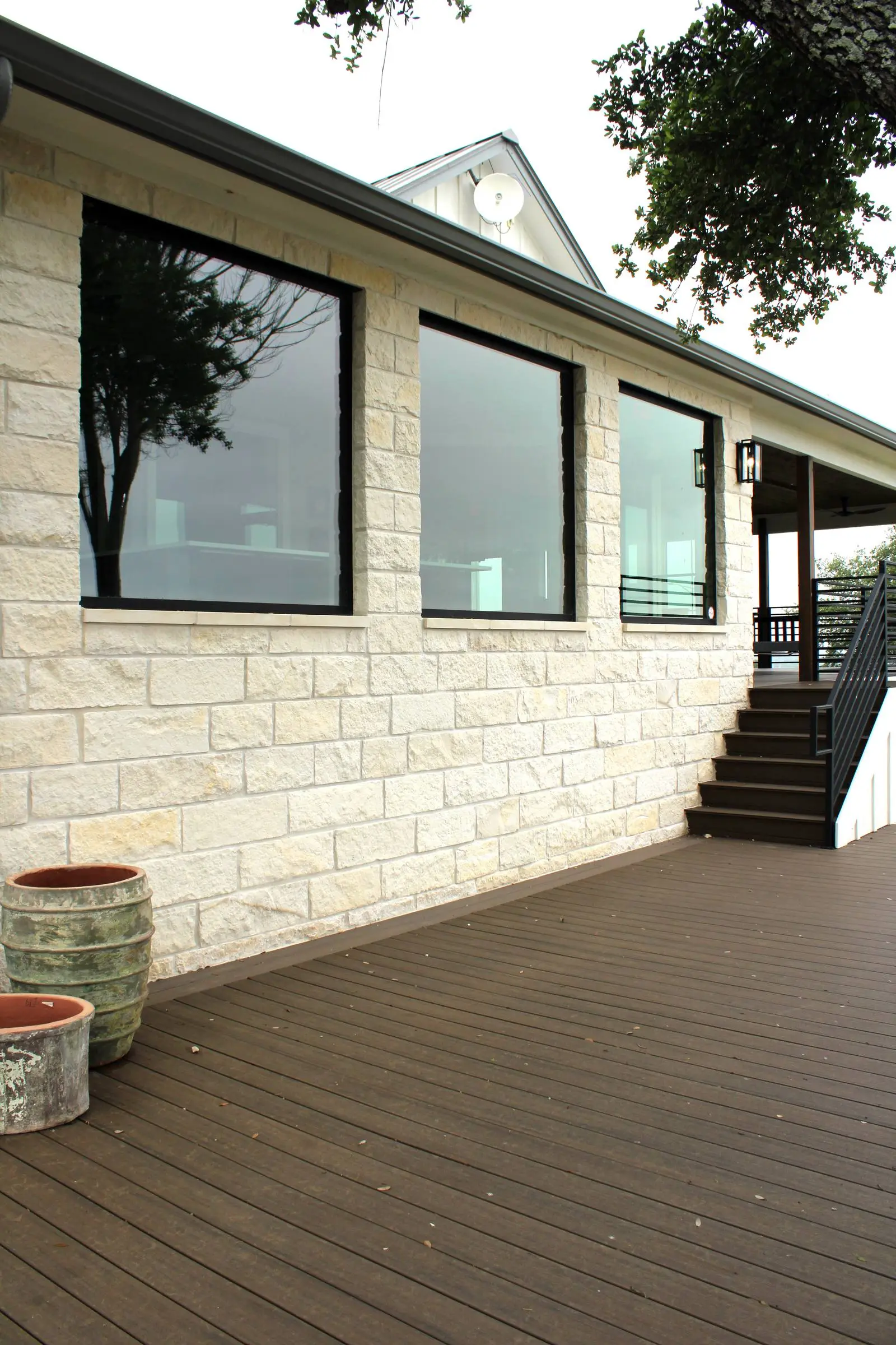 Three black-framed picture windows set into the limestone wall of a Hill Country home, seen from the deck that runs along the front.