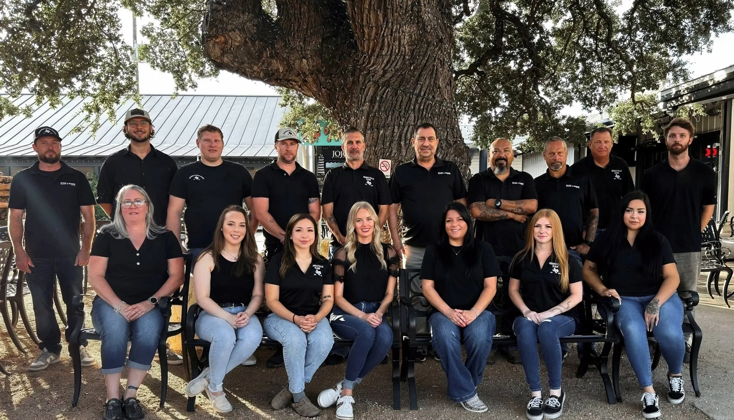 The Marble Falls Glass crew, around twenty people in black company shirts, gathered under a live oak outside the shop.